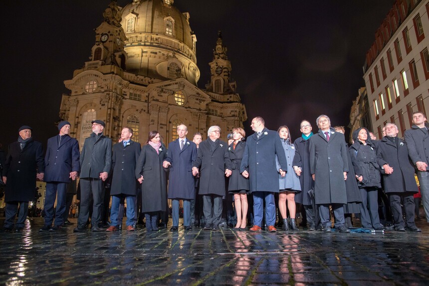 Männer und Frauen bilden vor der Frauenkirche in Dresden eine Menschenkette.